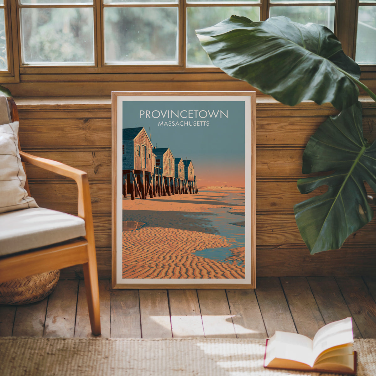 Cape Cod cottages print in an oak frame on sunlit wood panelling beside a mid-century armchair
