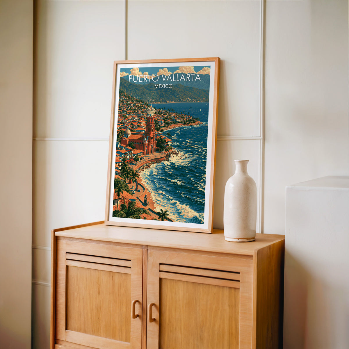 Mexican bay artwork in an oak frame on a light oak cabinet against a cream panelled wall, tall vase