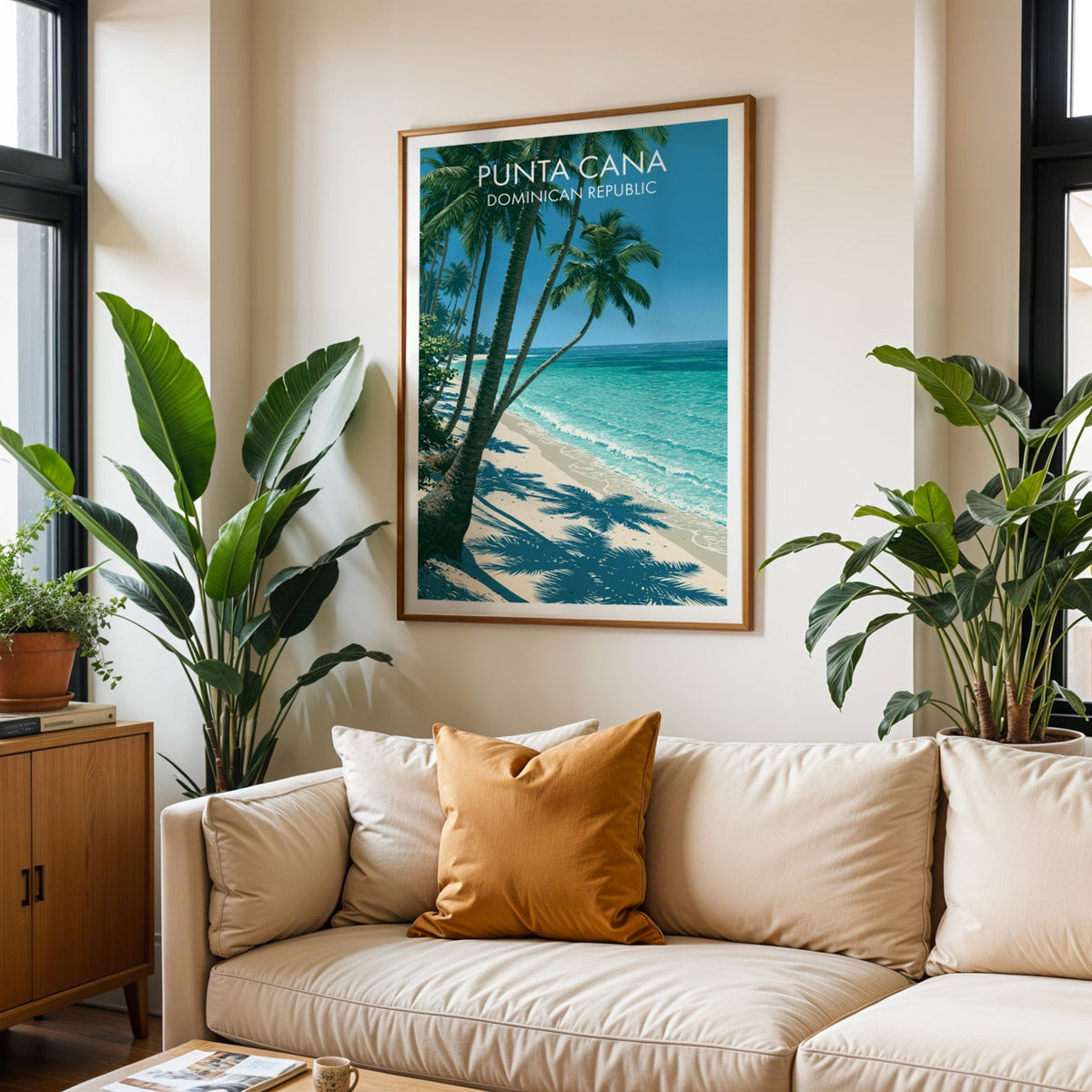 Caribbean beach print in an oak frame above a cream sofa with a burnt-orange cushion and tall tropical plants