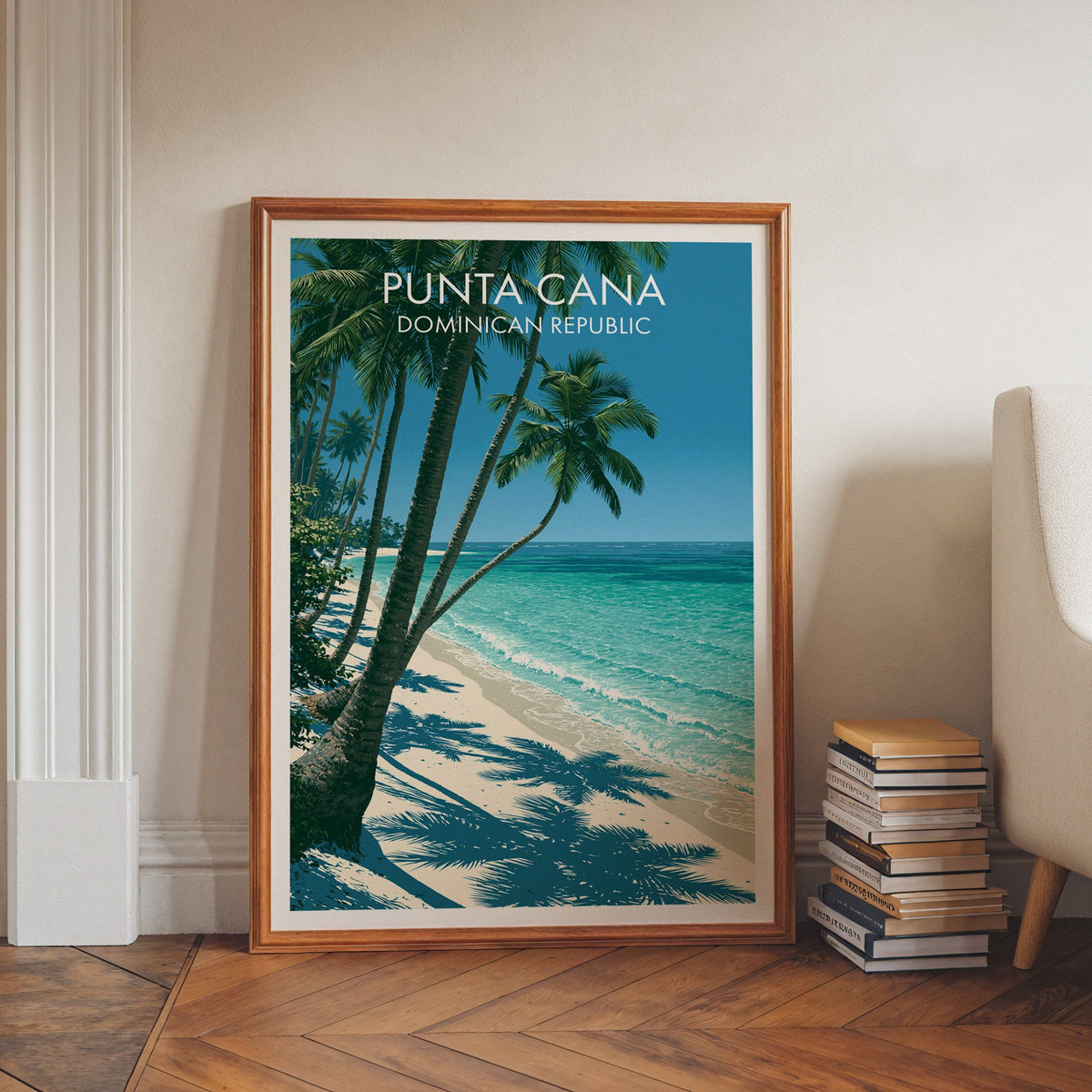 Blue and sand-toned beach print in a walnut frame leaning on herringbone floor beside stacked books
