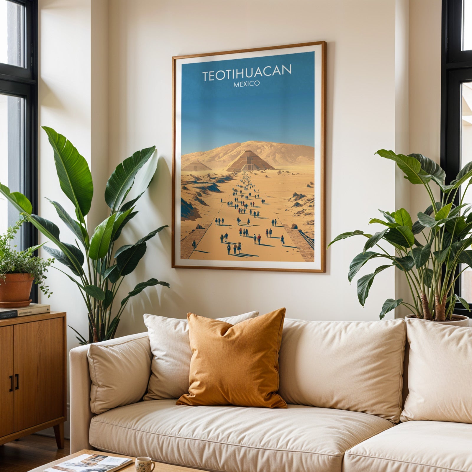 Mexico ruins poster in an oak frame above a cream sofa with a burnt-orange cushion and tall tropical plants