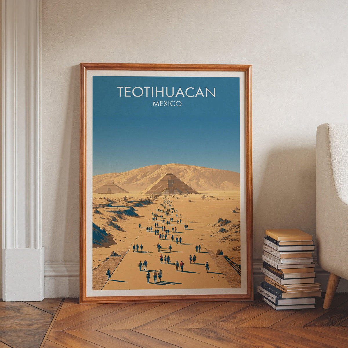Gold and dusty blue travel art in a walnut frame on herringbone floor beside stacked books