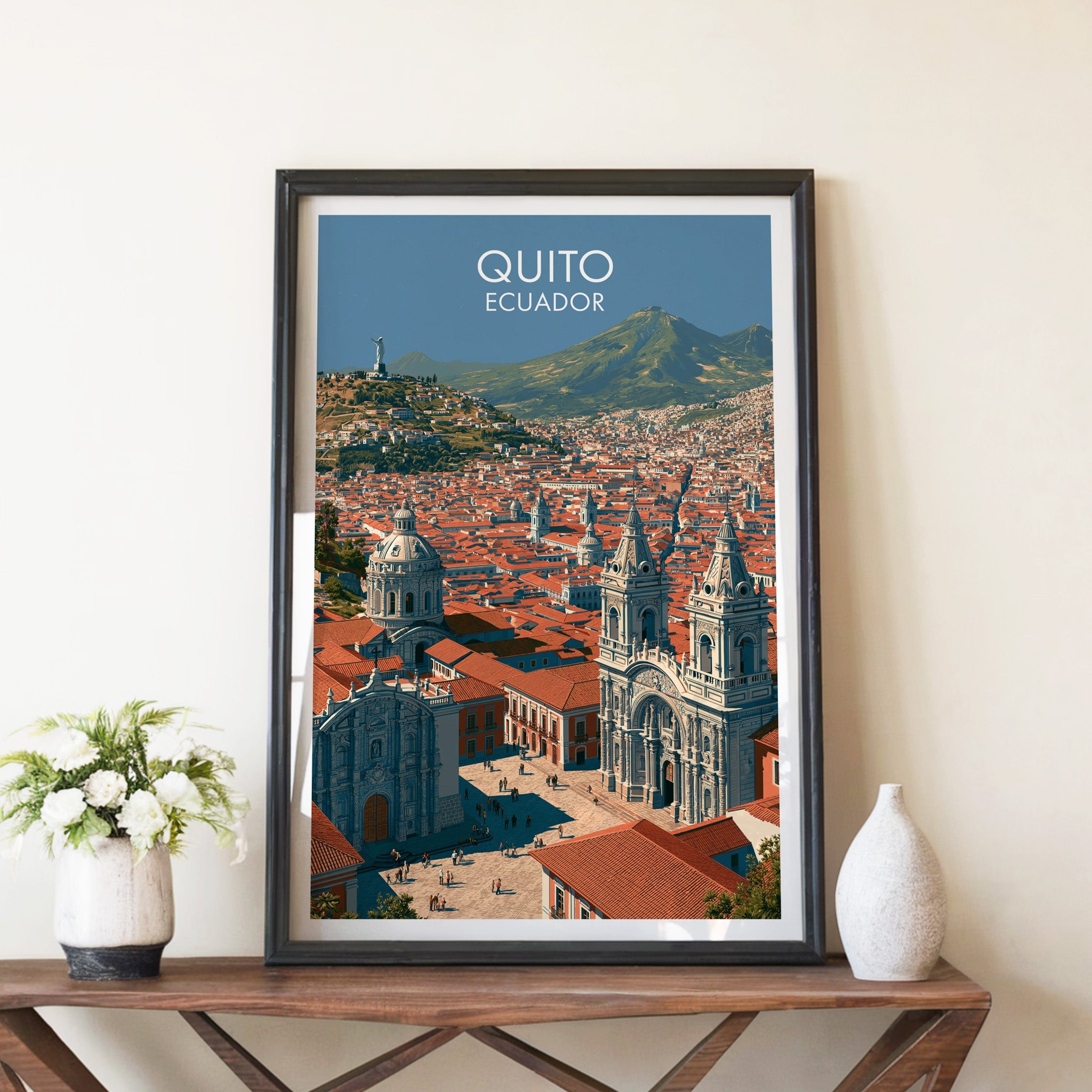 Quito old town poster in a black frame on a brown X-leg console with white blooms and a pale ceramic vase