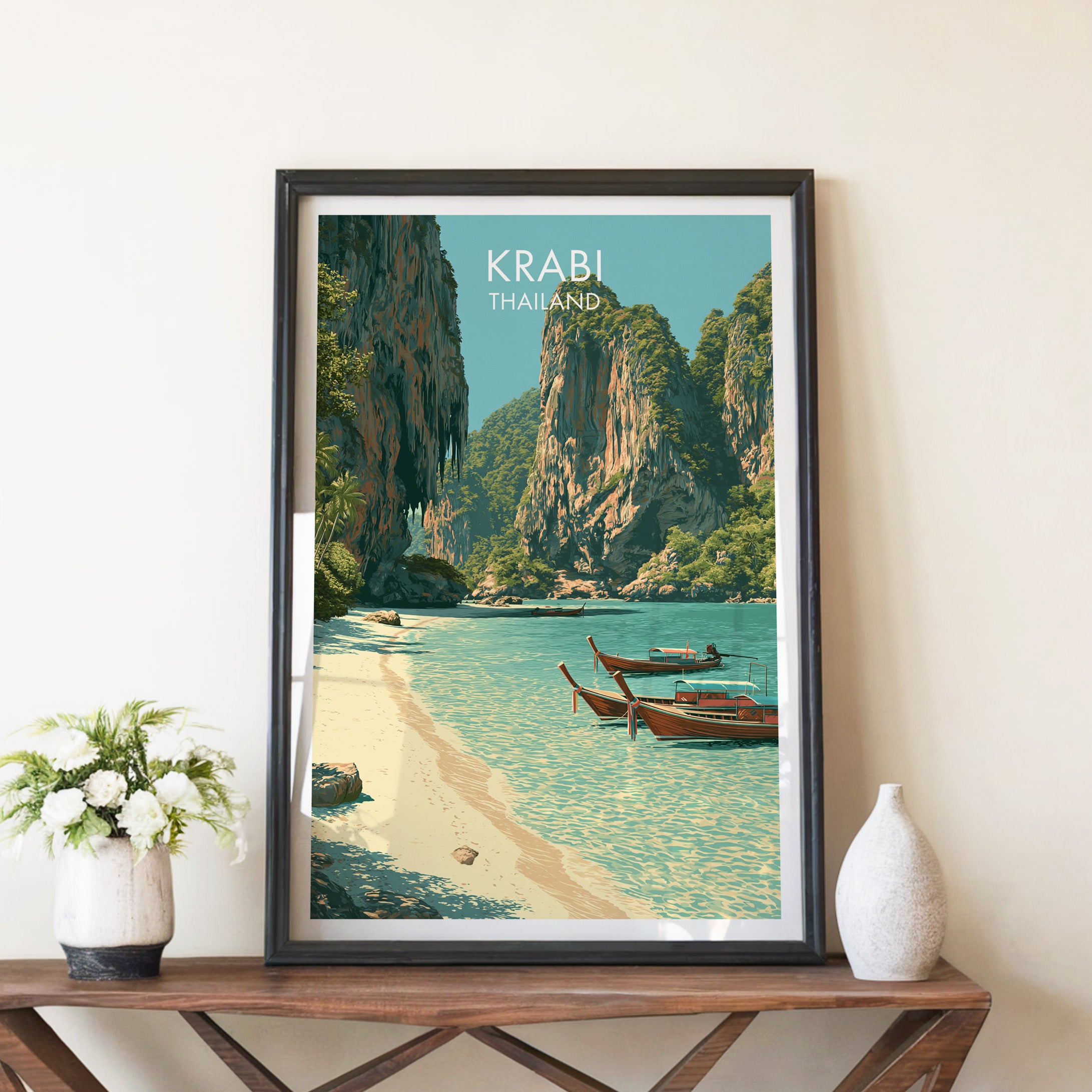 Railay Beach Krabi Thailand travel poster in a black frame on a wooden console table with white flowers