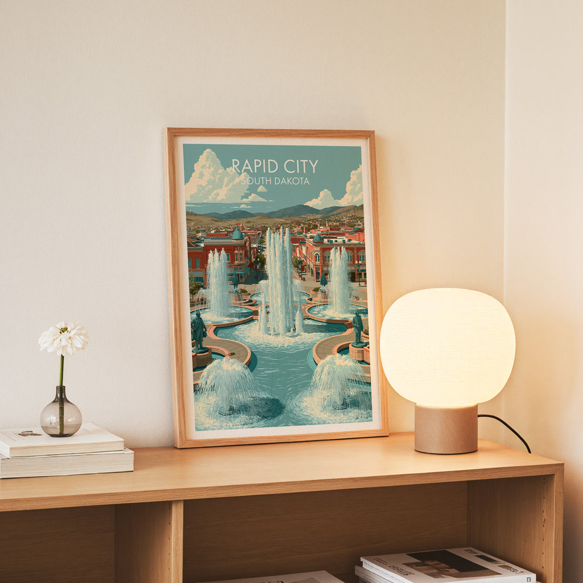 Rapid City print in a slim oak frame standing on a console with white daisies in a glass jar.