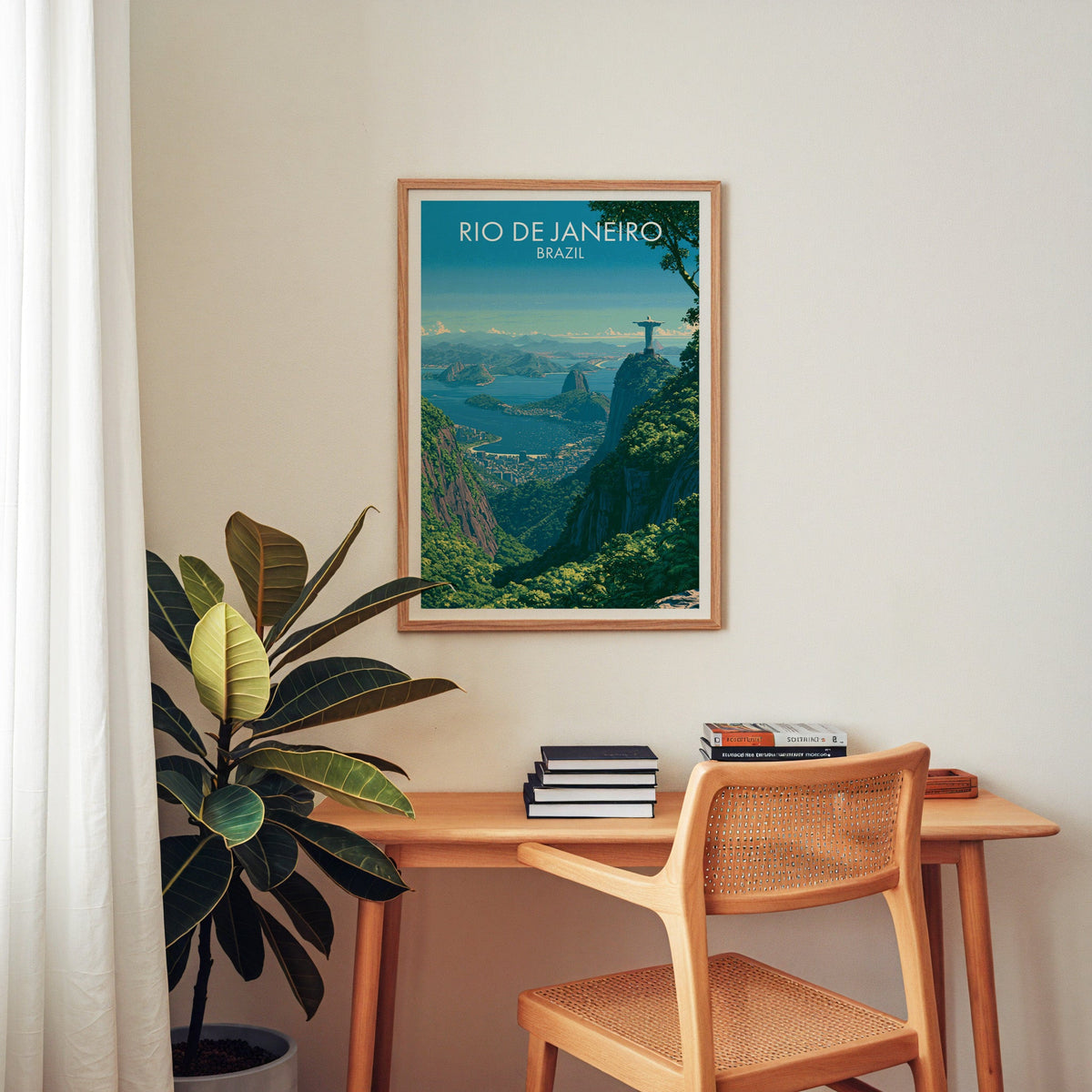 Rio de Janeiro travel art in an oak frame over a wood desk with a cane chair, stacked books and a rubber plant