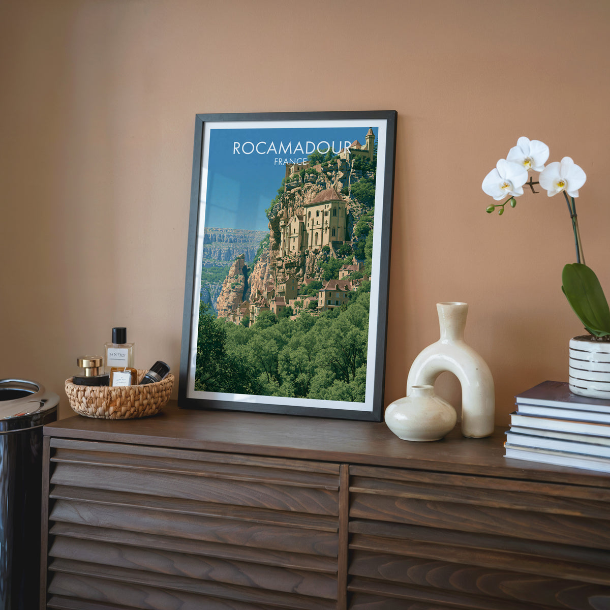 Rocamadour France wall art, black frame on a walnut sideboard against a terracotta wall with a white orchid