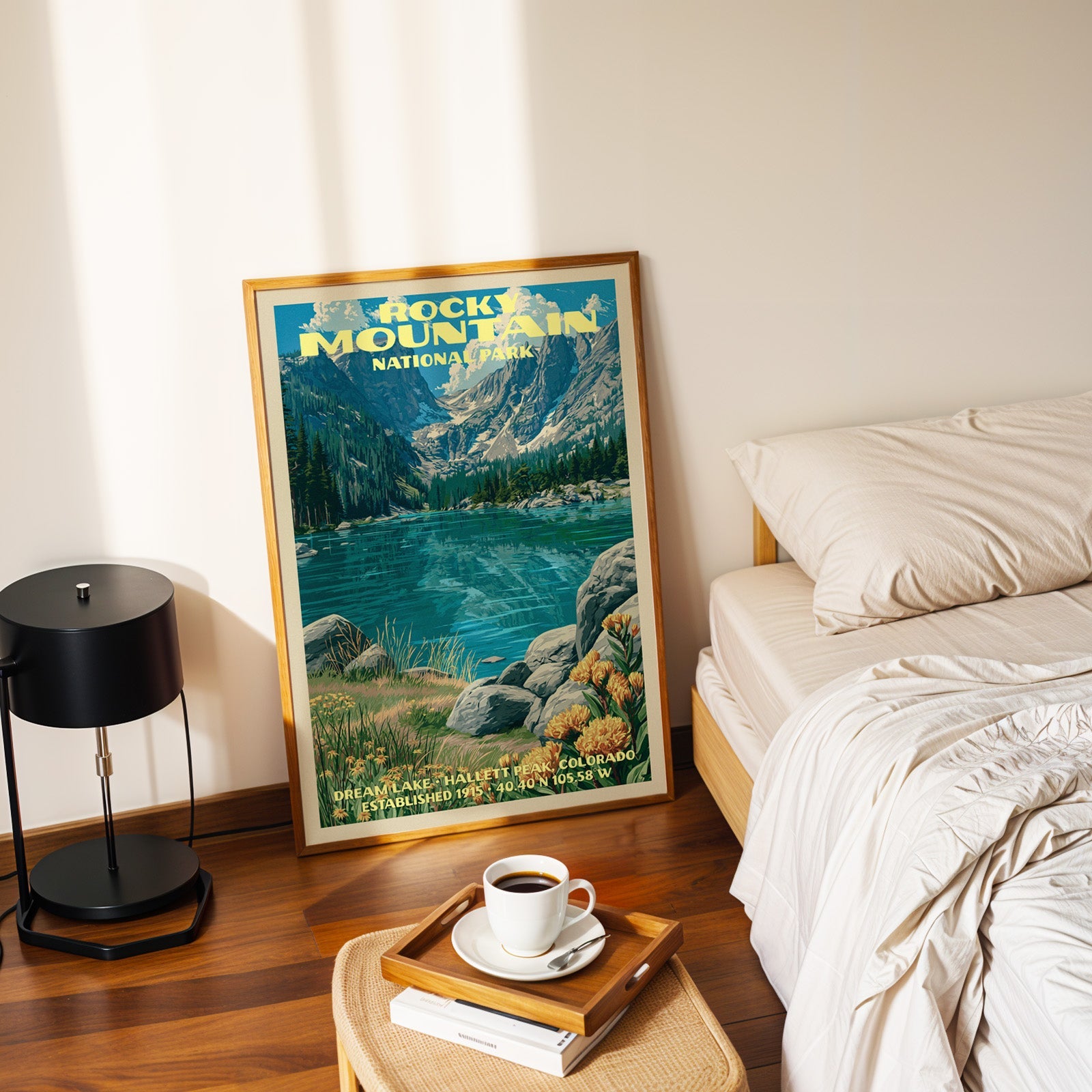 Dream Lake Rocky Mountain print in a gold frame on the floor beside a made bed and a black table lamp
