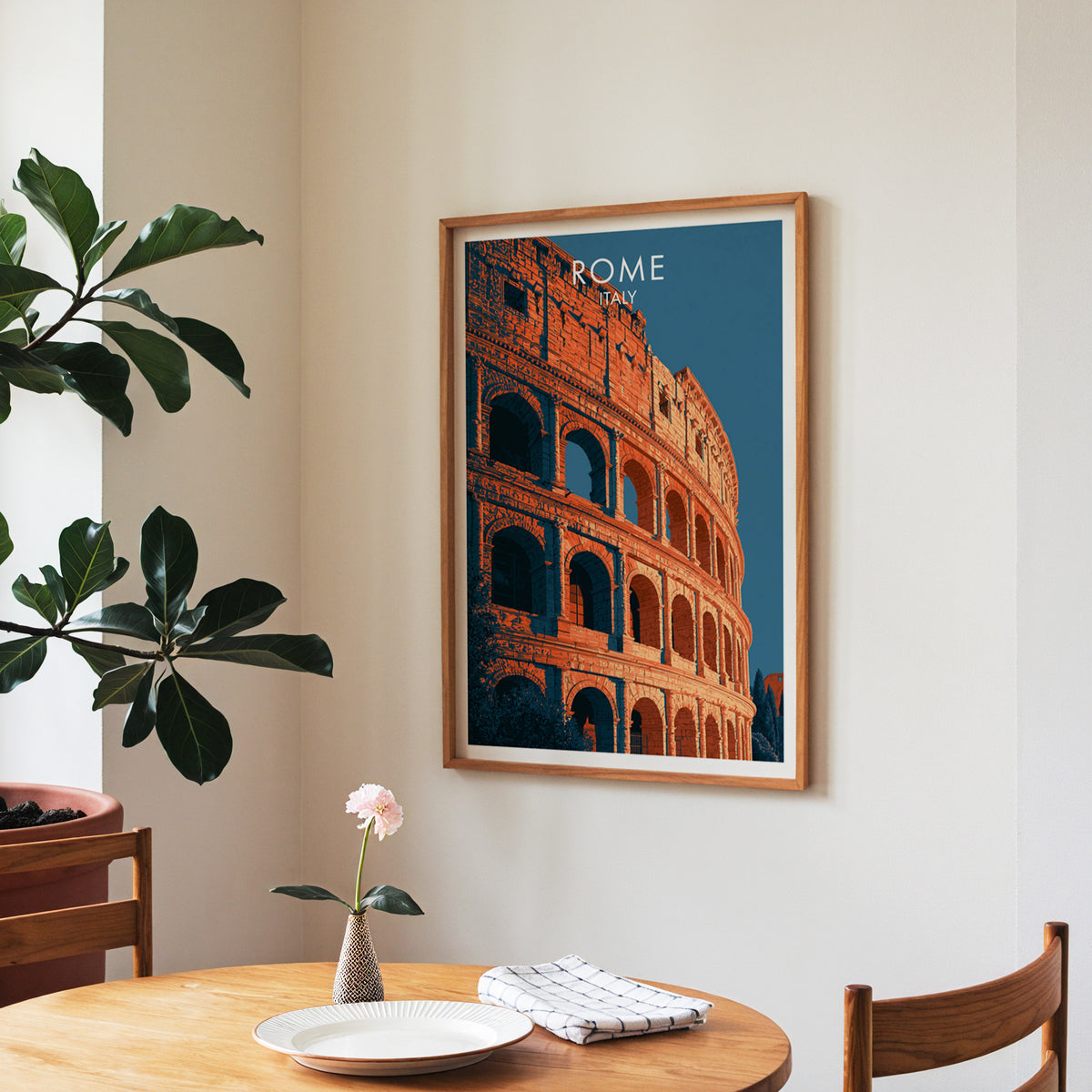 Rome travel wall art in a walnut frame over a round dining table with a plate, napkin and a rose