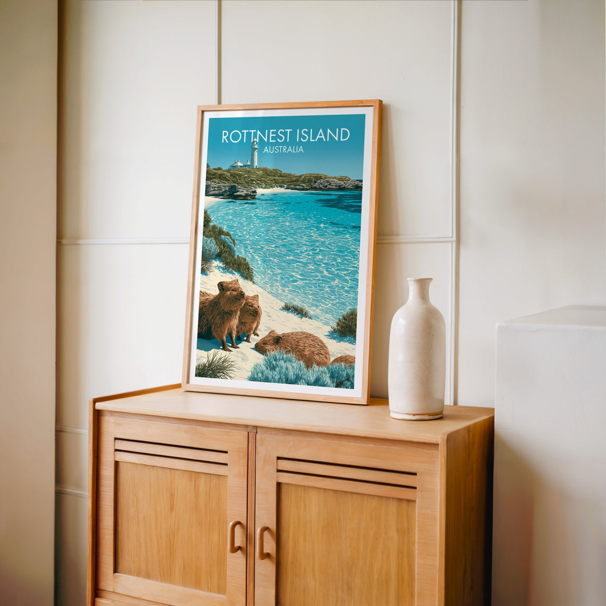 Island lighthouse travel print in an oak frame on a light oak cabinet by a cream panelled wall