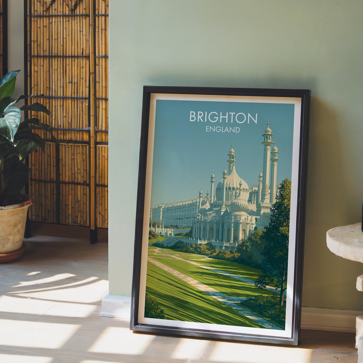 Brighton lawns poster, dark frame leaning on a sage-green wall beside a bamboo screen and a peace lily