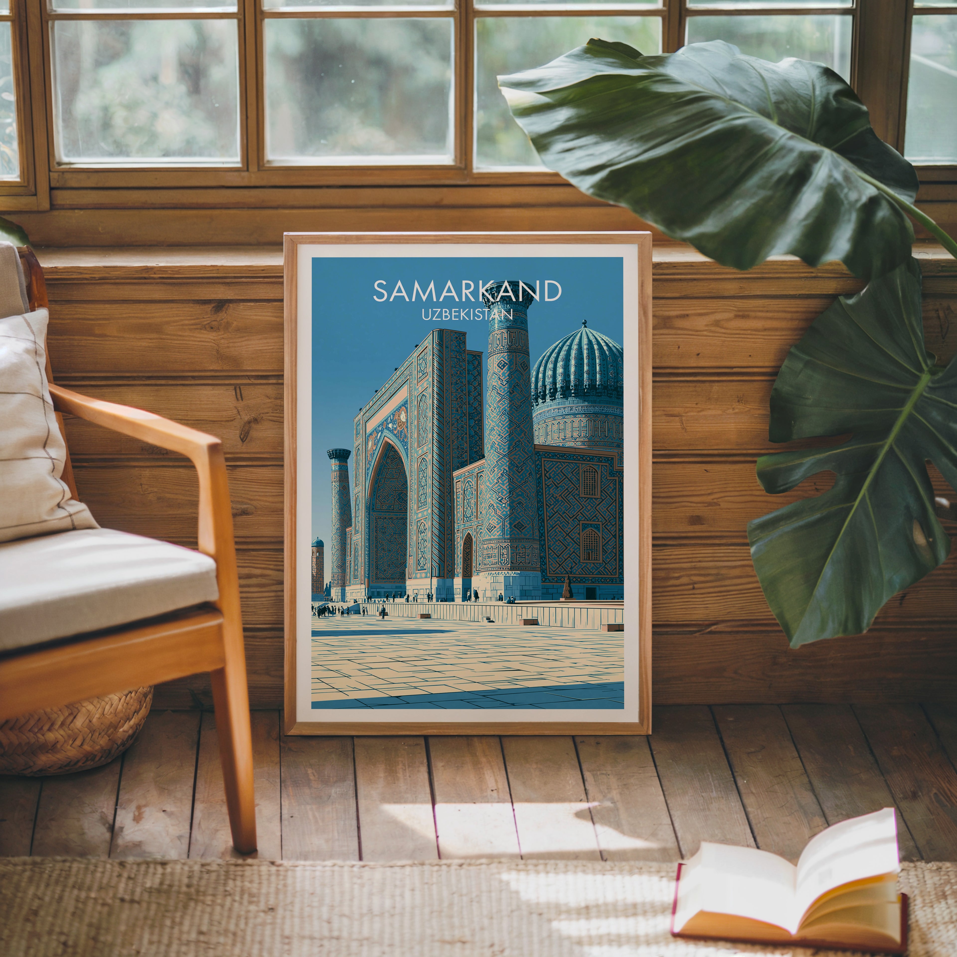 Framed Samarkand Uzbekistan poster leaning against a timber cabin wall with monstera leaves and an open book