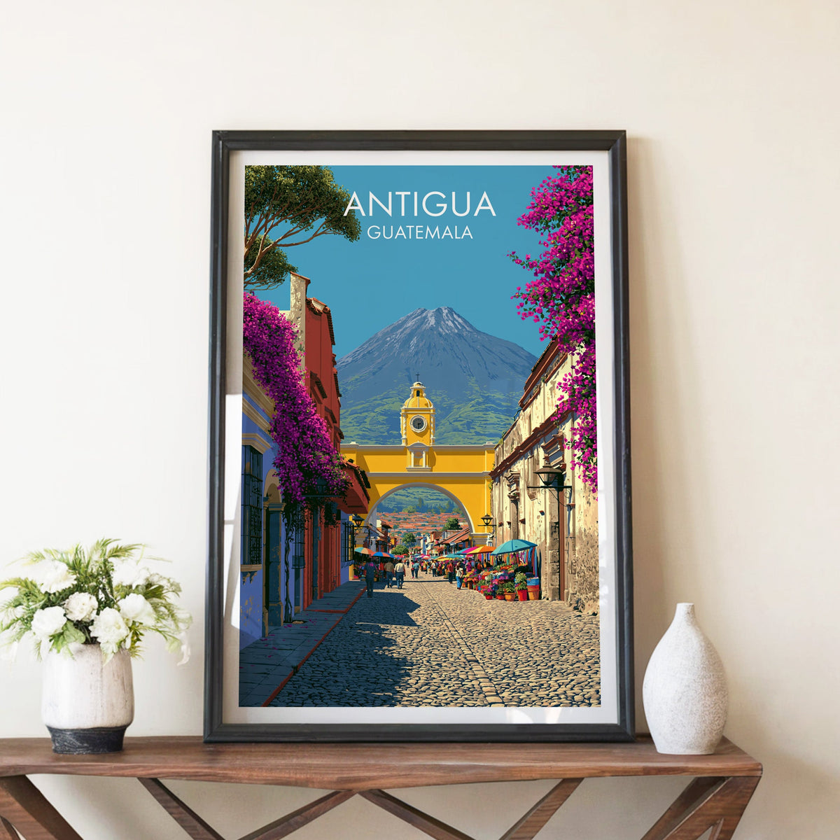 Yellow clock arch over a cobbled street, black frame on a walnut console with white peonies and a ceramic vase