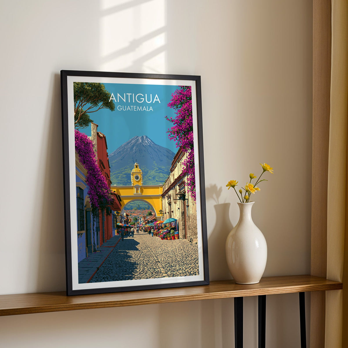 Bougainvillea and a mustard archway in a black frame on a wood shelf, yellow daisies against a sunlit cream wall