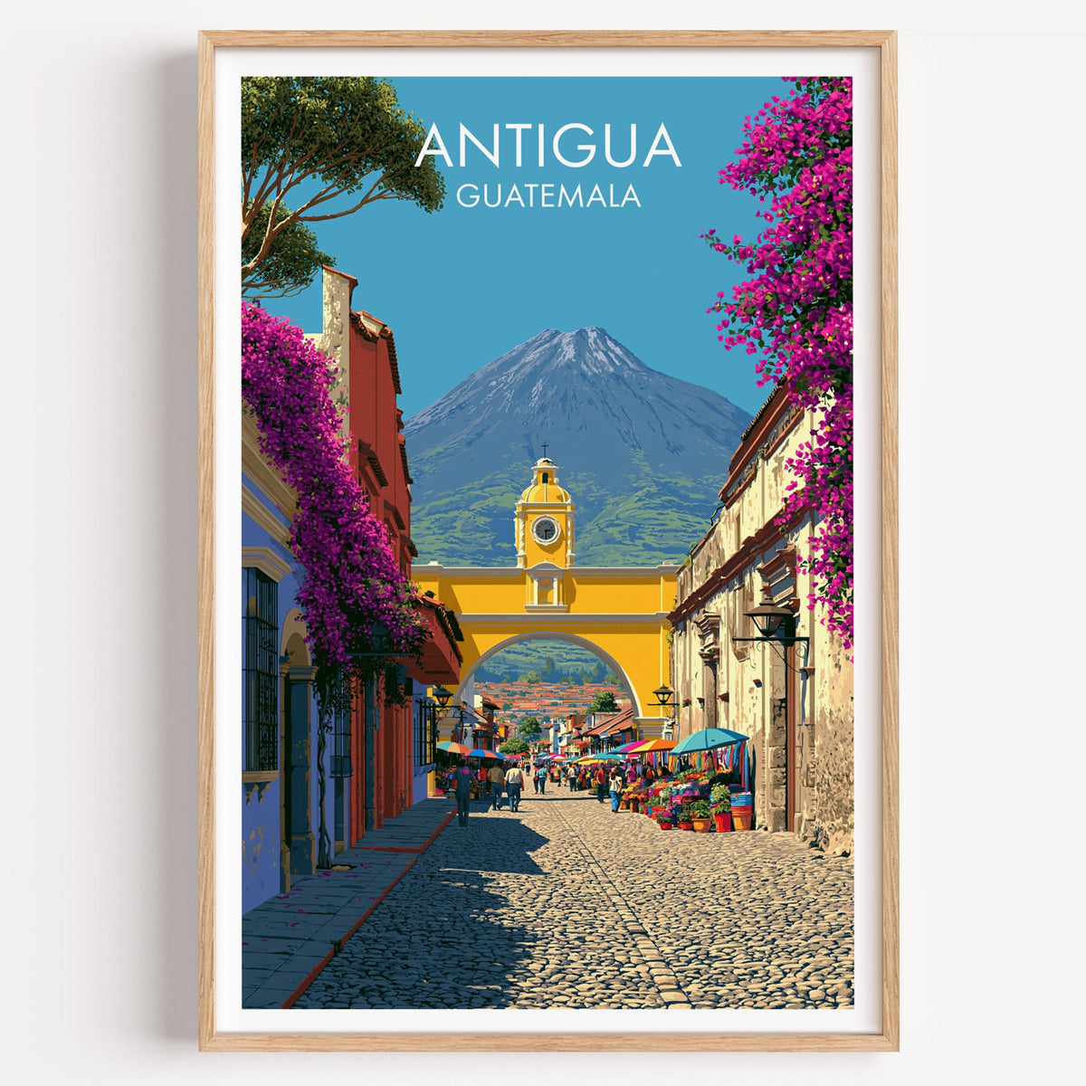 Antigua Guatemala travel print in a light oak frame on a plain white wall, yellow arch and volcano beyond