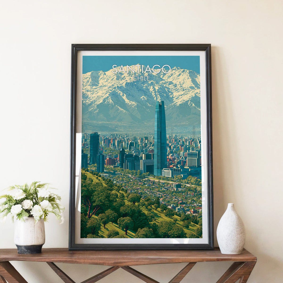 Santiago skyline print in a black frame leaning on a brown wood console with white flowers in a ceramic vase