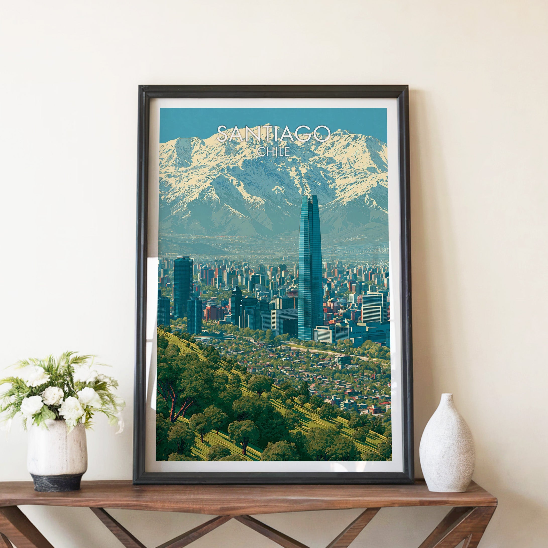 Santiago skyline print in a black frame leaning on a brown wood console with white flowers in a ceramic vase