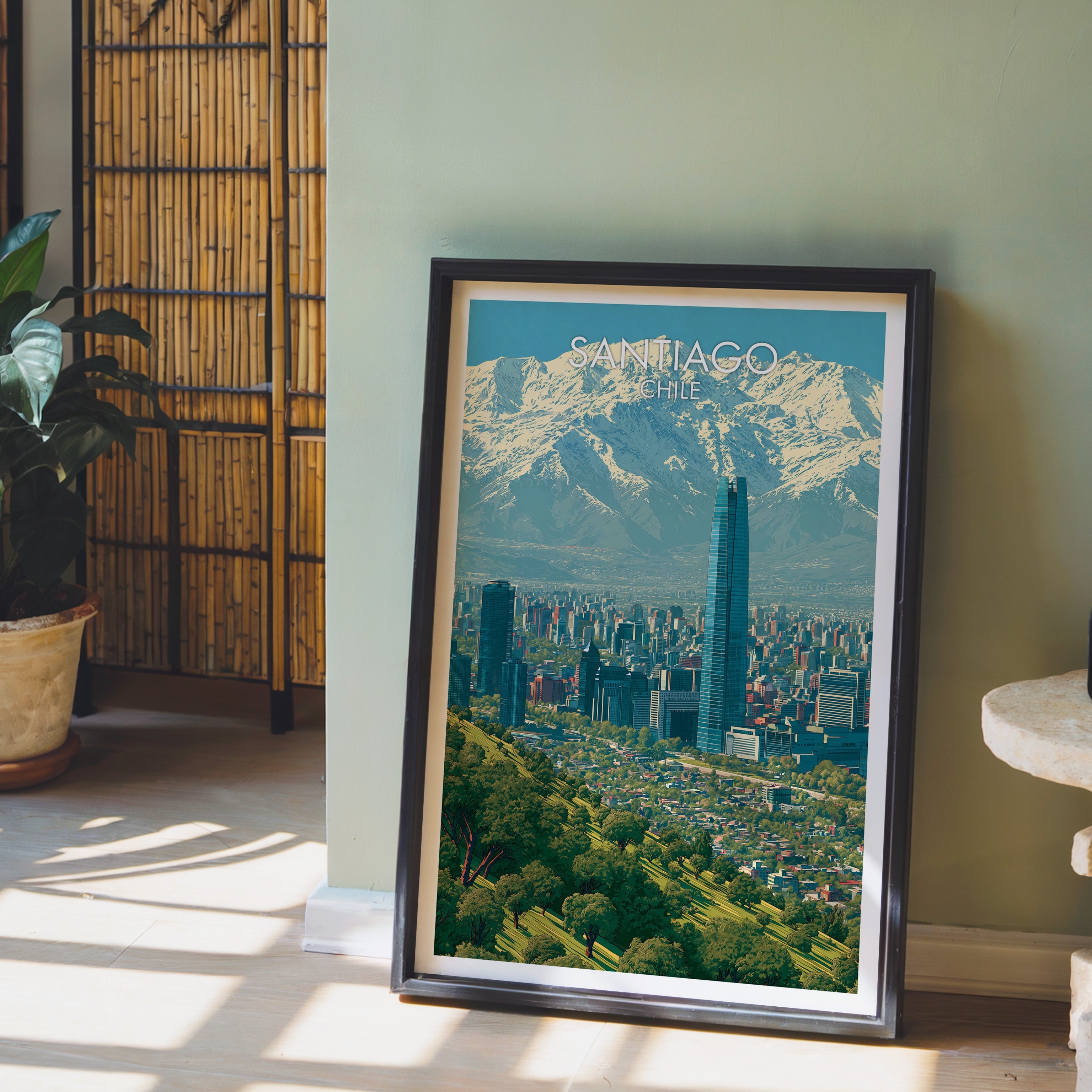 Andes and Santiago city print in a dark brown frame on a light wood floor by a sage wall, bamboo screen and potted plant