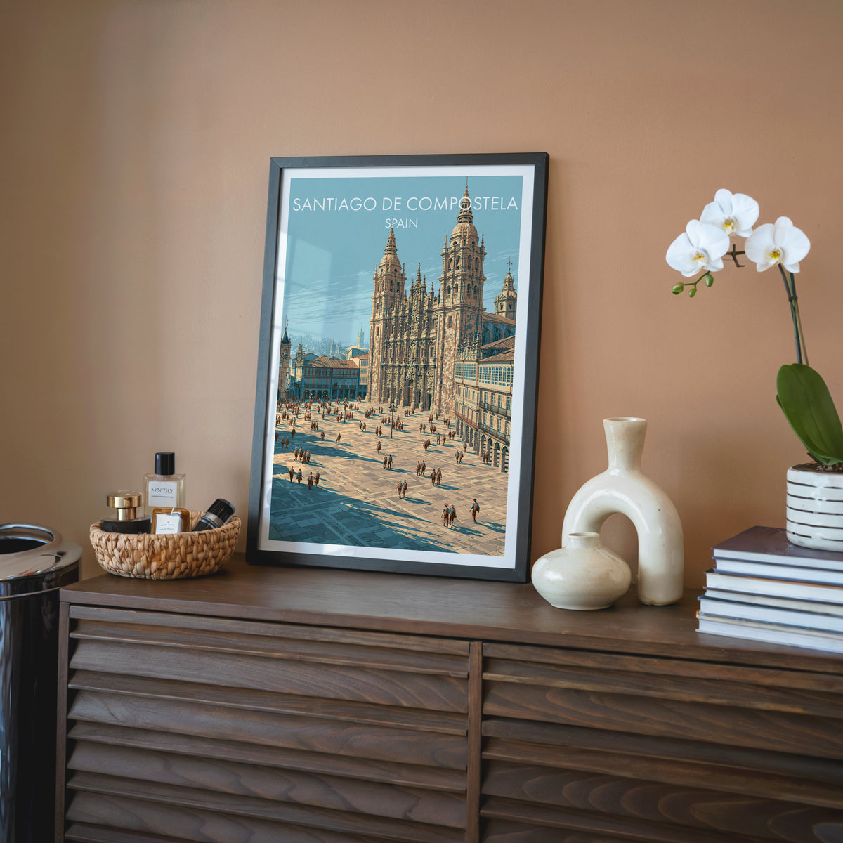 Santiago de Compostela wall art, black frame on a walnut sideboard against a terracotta wall with a white orchid