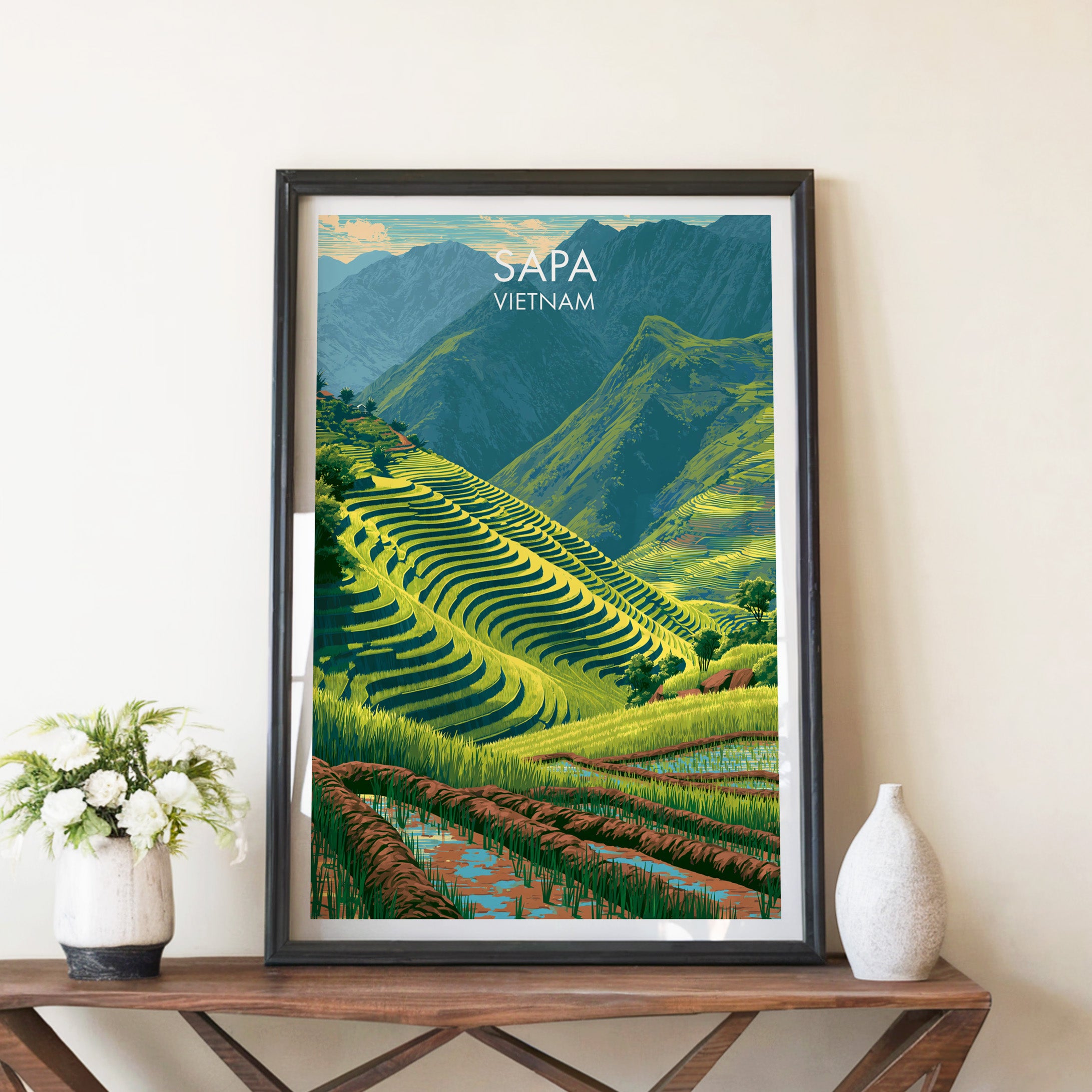 Sapa Vietnam travel poster in a black frame on a wooden console table with white flowers