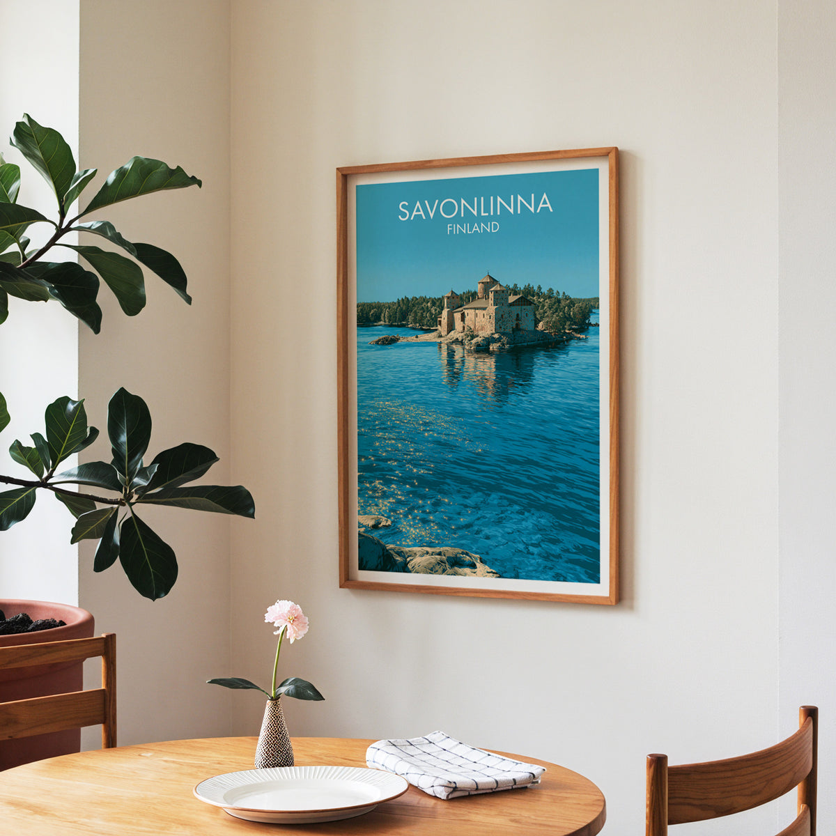 Savonlinna island fortress poster, walnut frame in a dining corner above a round table and a fiddle-leaf fig