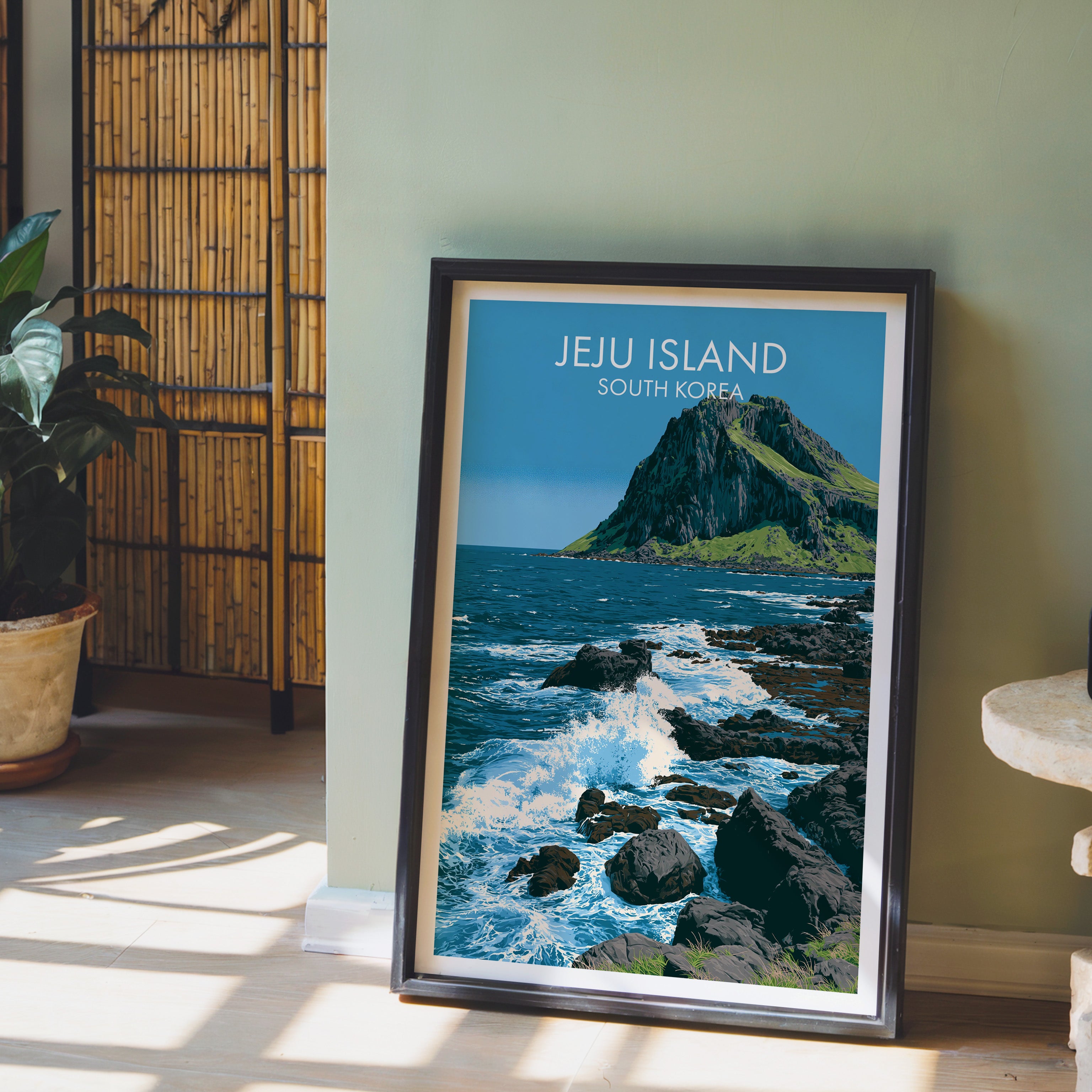 Seongsan Ilchulbong Jeju Korea wall art in a black frame leaning against a sage green wall beside a bamboo screen