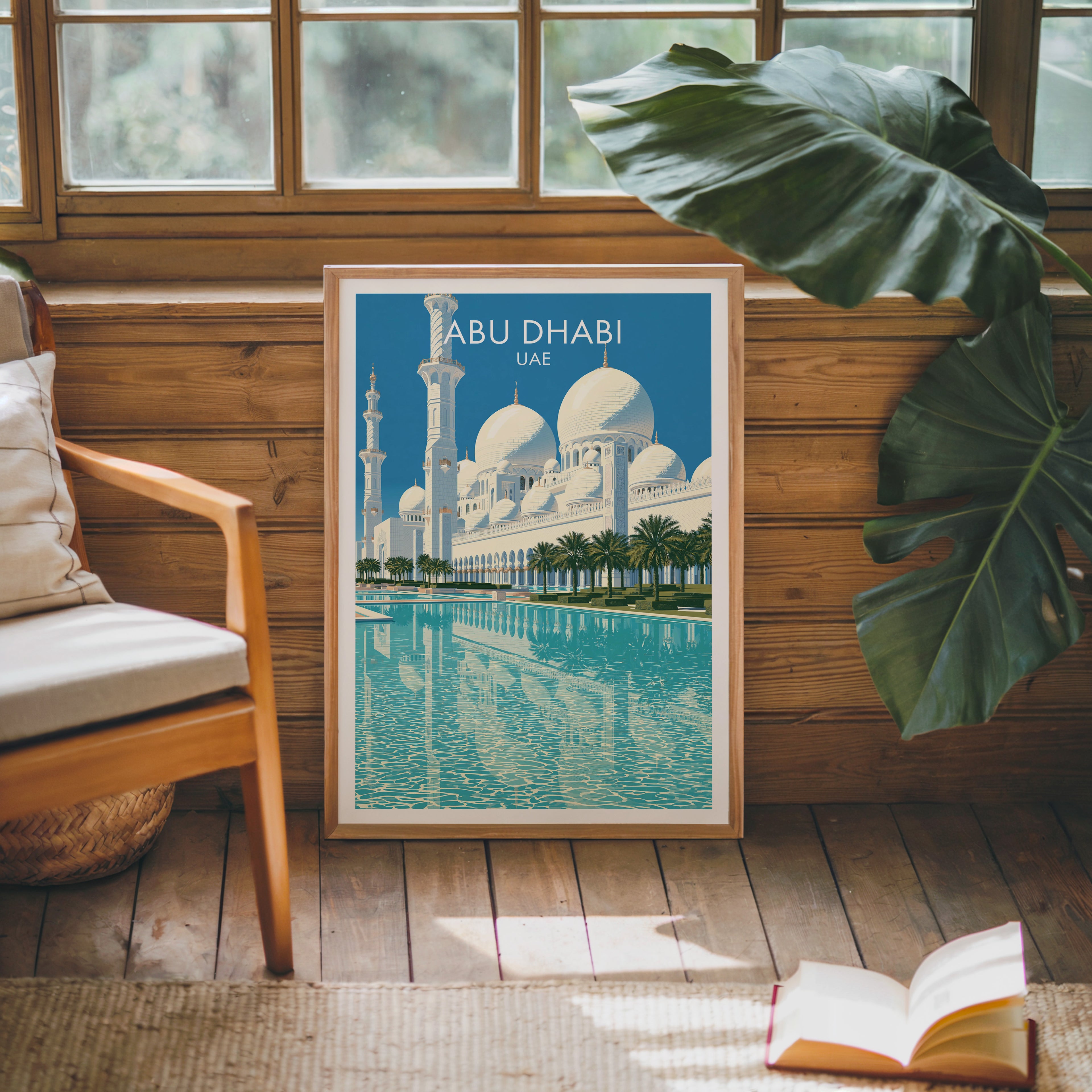Framed Sheikh Zayed Mosque Abu Dhabi poster leaning against a timber cabin wall with monstera leaves and an open book
