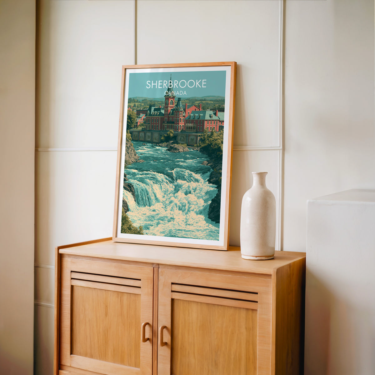 Sherbrooke brick clock tower art in an oak frame on a light wood cabinet beside a stoneware vase