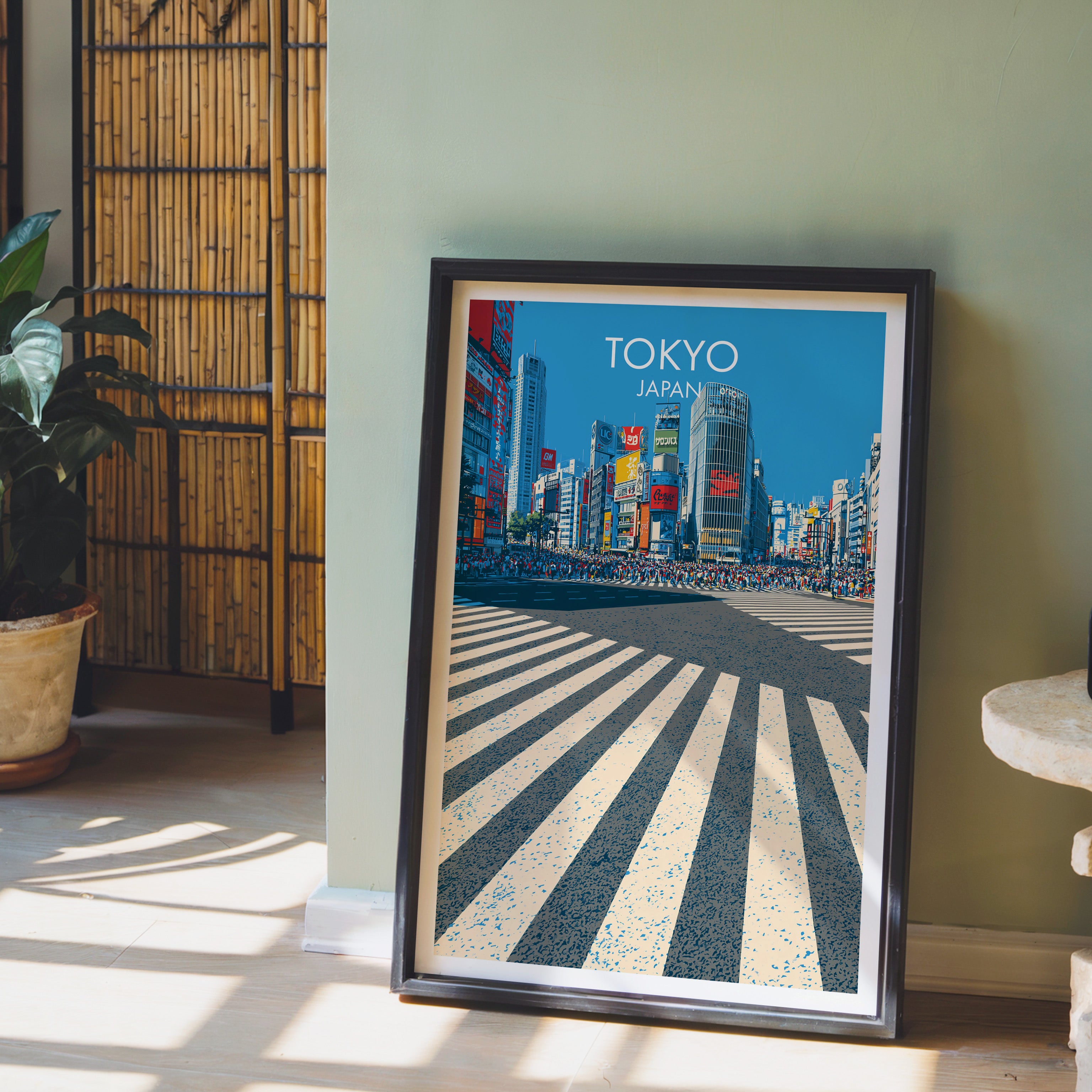 Shibuya Crossing Tokyo Japan wall art in a black frame leaning against a sage green wall beside a bamboo screen