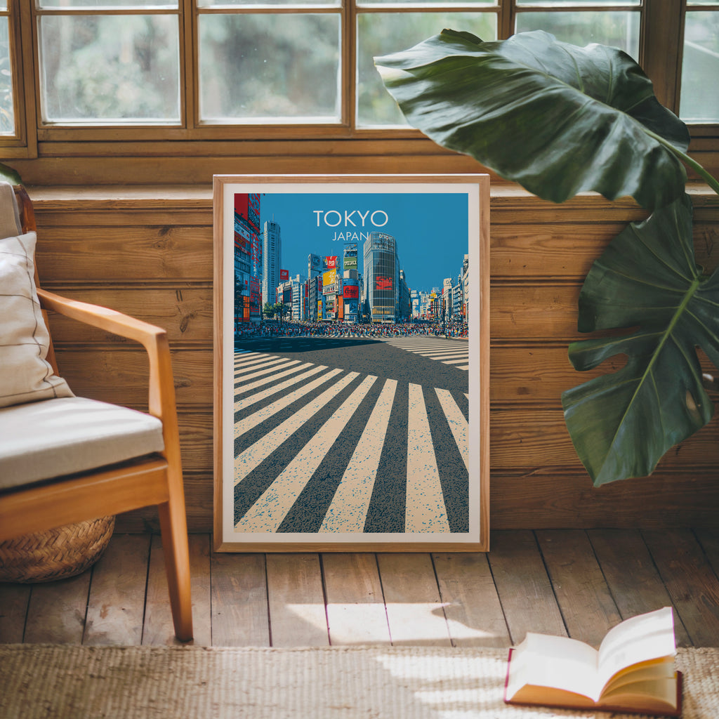 Framed Shibuya Crossing Tokyo Japan poster leaning against a timber cabin wall with monstera leaves and an open book
