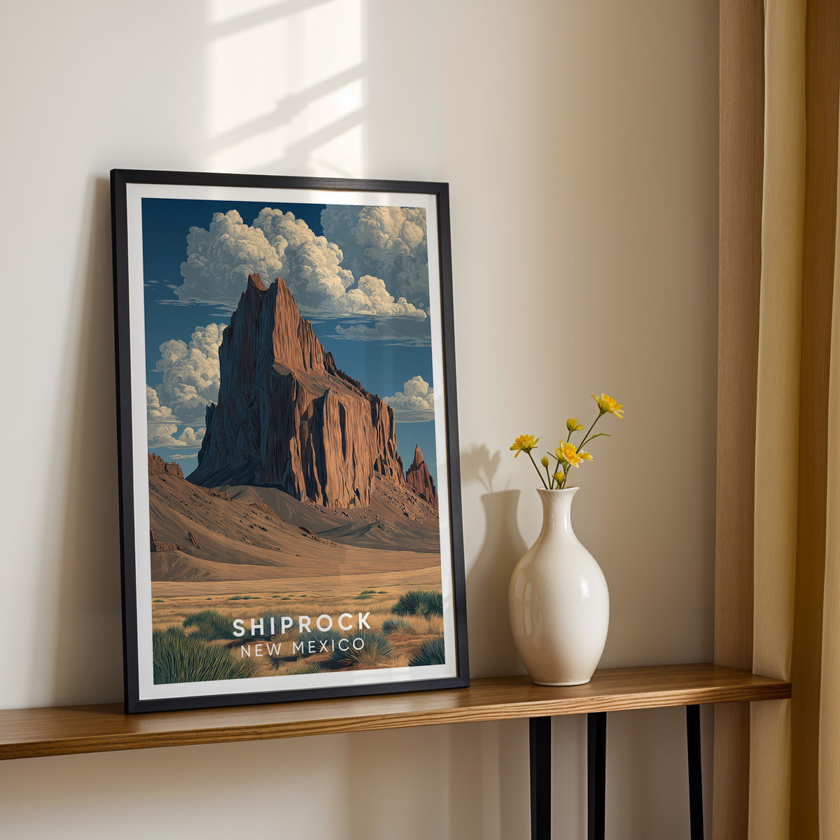 Shiprock print in a black frame on a narrow wood console, sunlit white vase of yellow flowers beside it