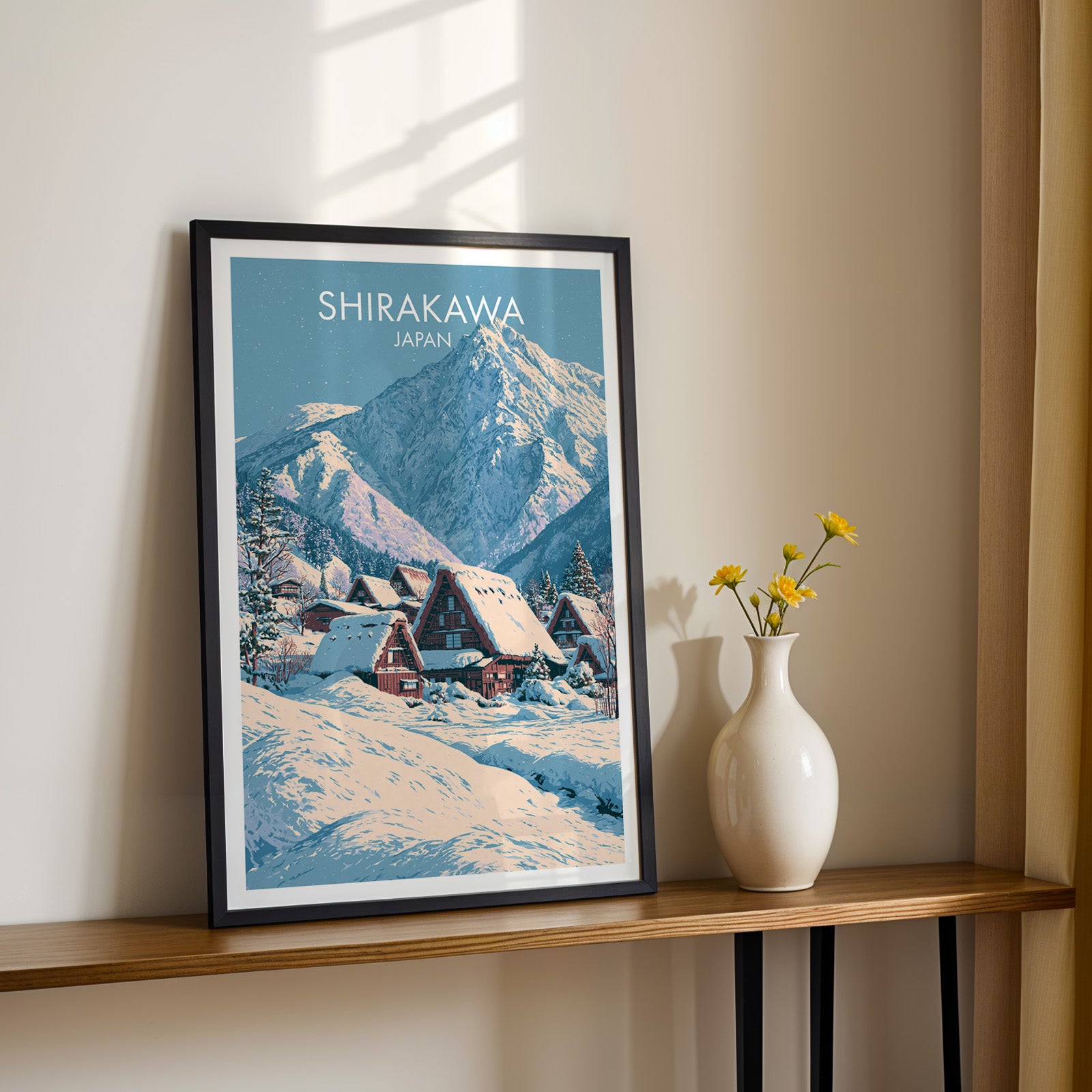 Black framed Shirakawa go Japan print on a narrow hallway console in sunlight, styled with yellow flowers