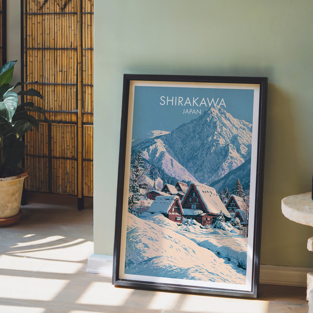 Shirakawa go Japan wall art in a black frame leaning against a sage green wall beside a bamboo screen