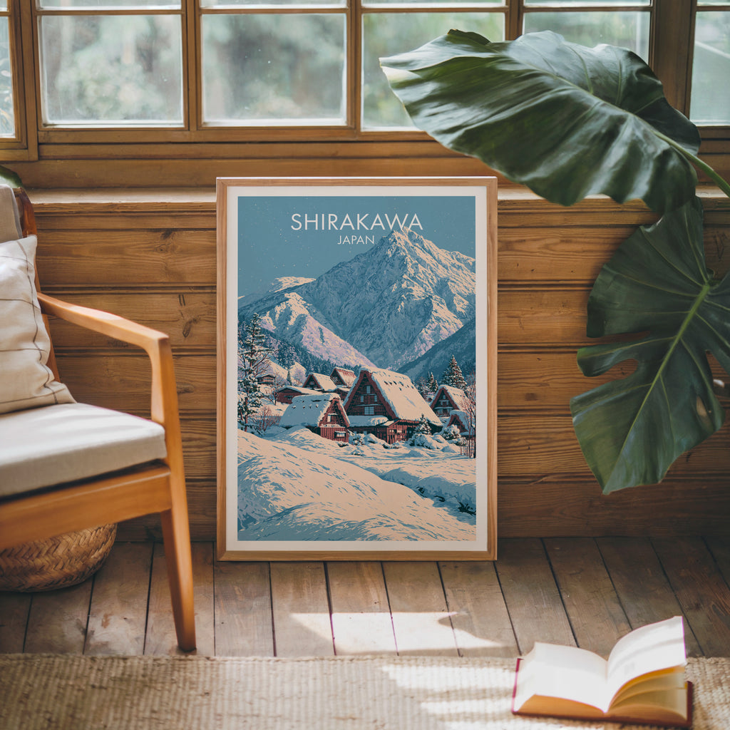 Framed Shirakawa go Japan poster leaning against a timber cabin wall with monstera leaves and an open book