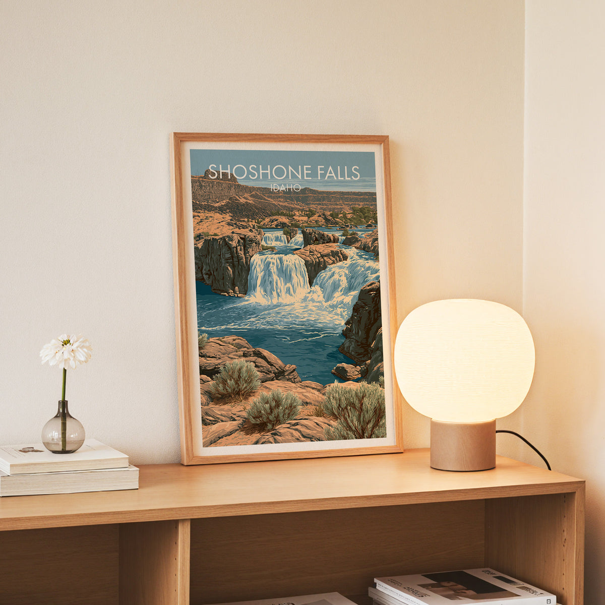 Idaho waterfall poster in a slim oak frame standing on a console with white daisies in a glass jar.