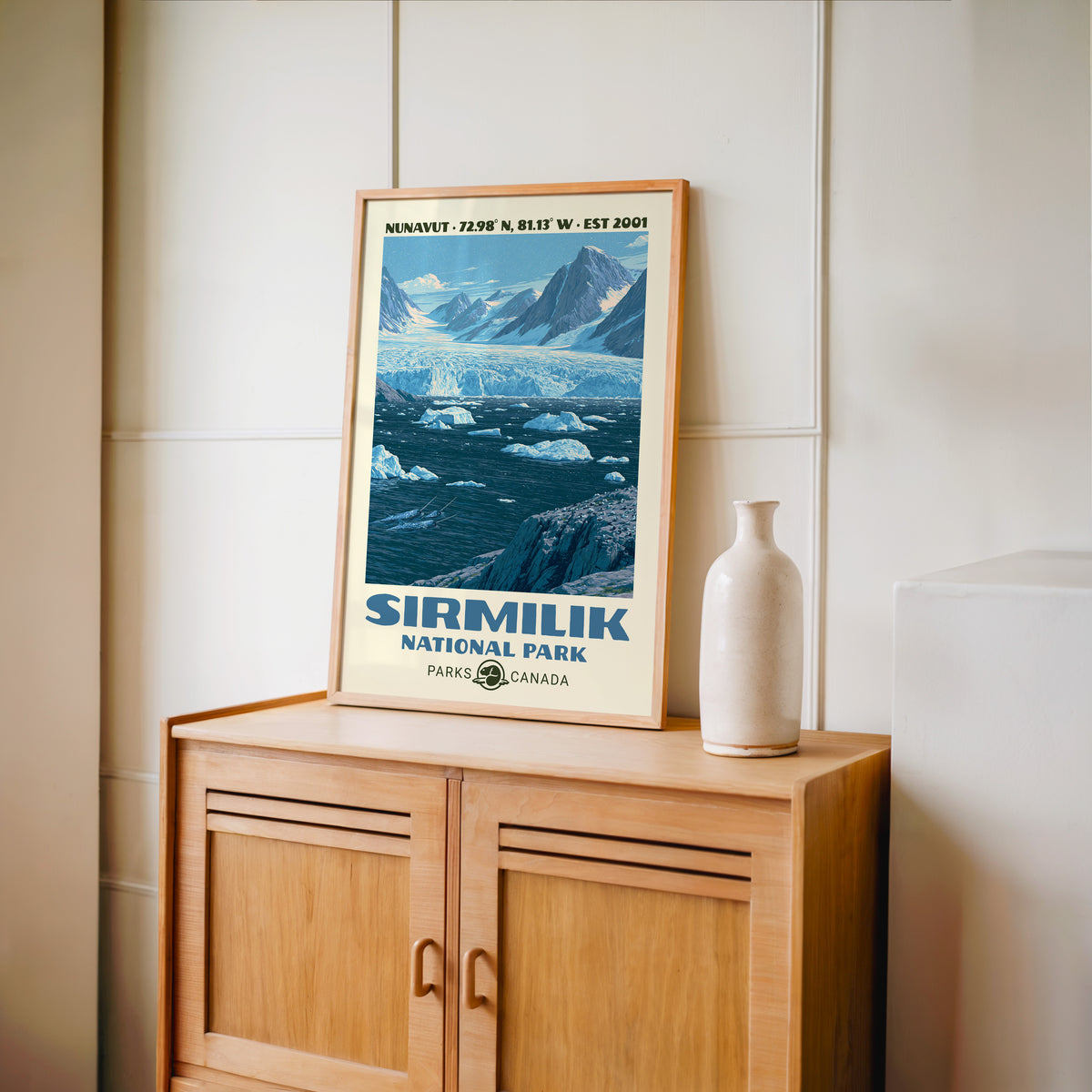 Sirmilik National Park wall art, Nunavut in an oak frame on a light wood cabinet beside a stoneware vase