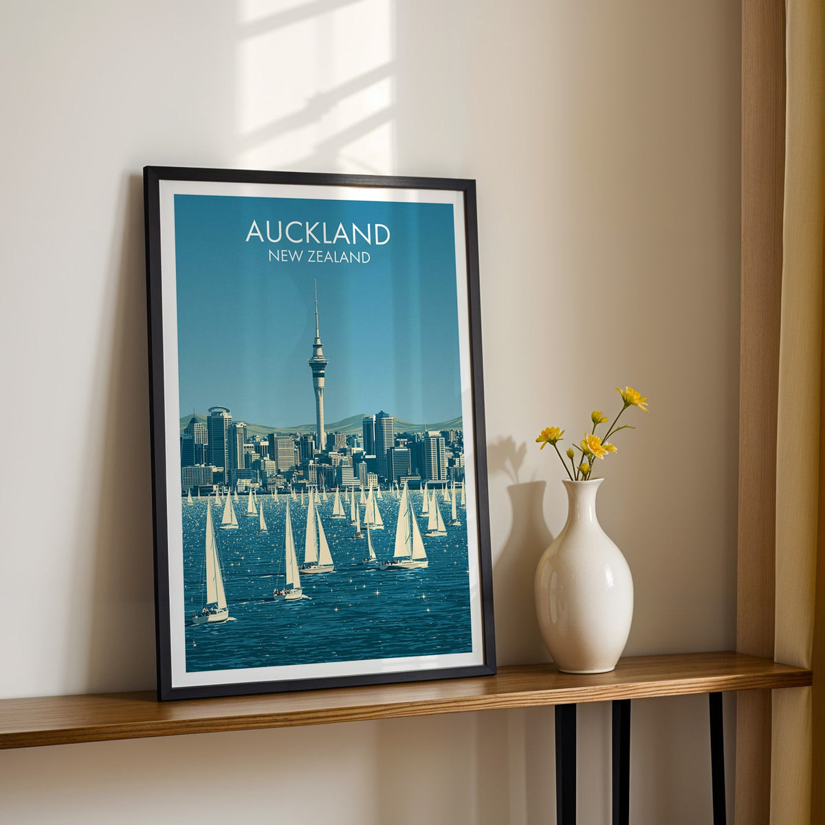 Sky Tower print in a black frame on a wood shelf with yellow daisies against a sunlit cream wall