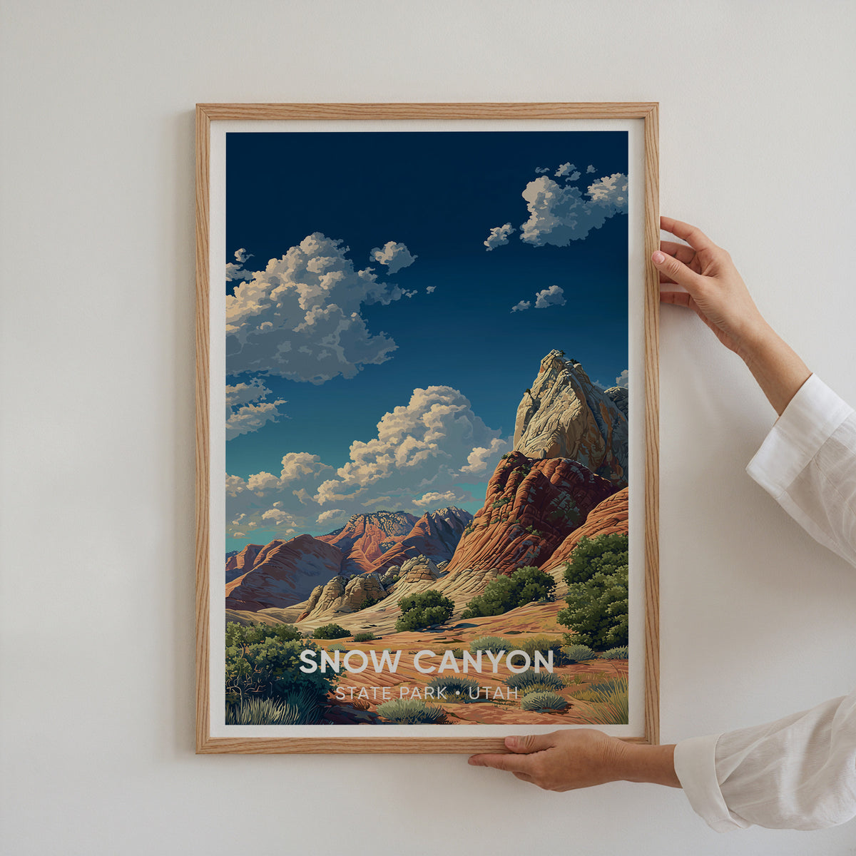 Two hands hold an oak-framed Snow Canyon sandstone print against a plain white wall