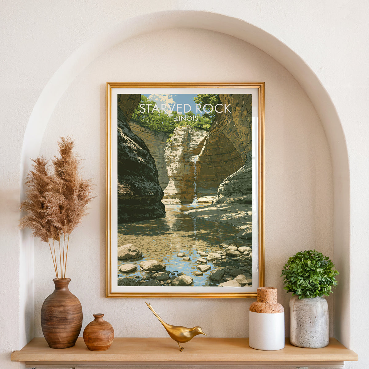 Gold-framed Illinois waterfall art in an arched wall niche with pampas grass and a brass bird