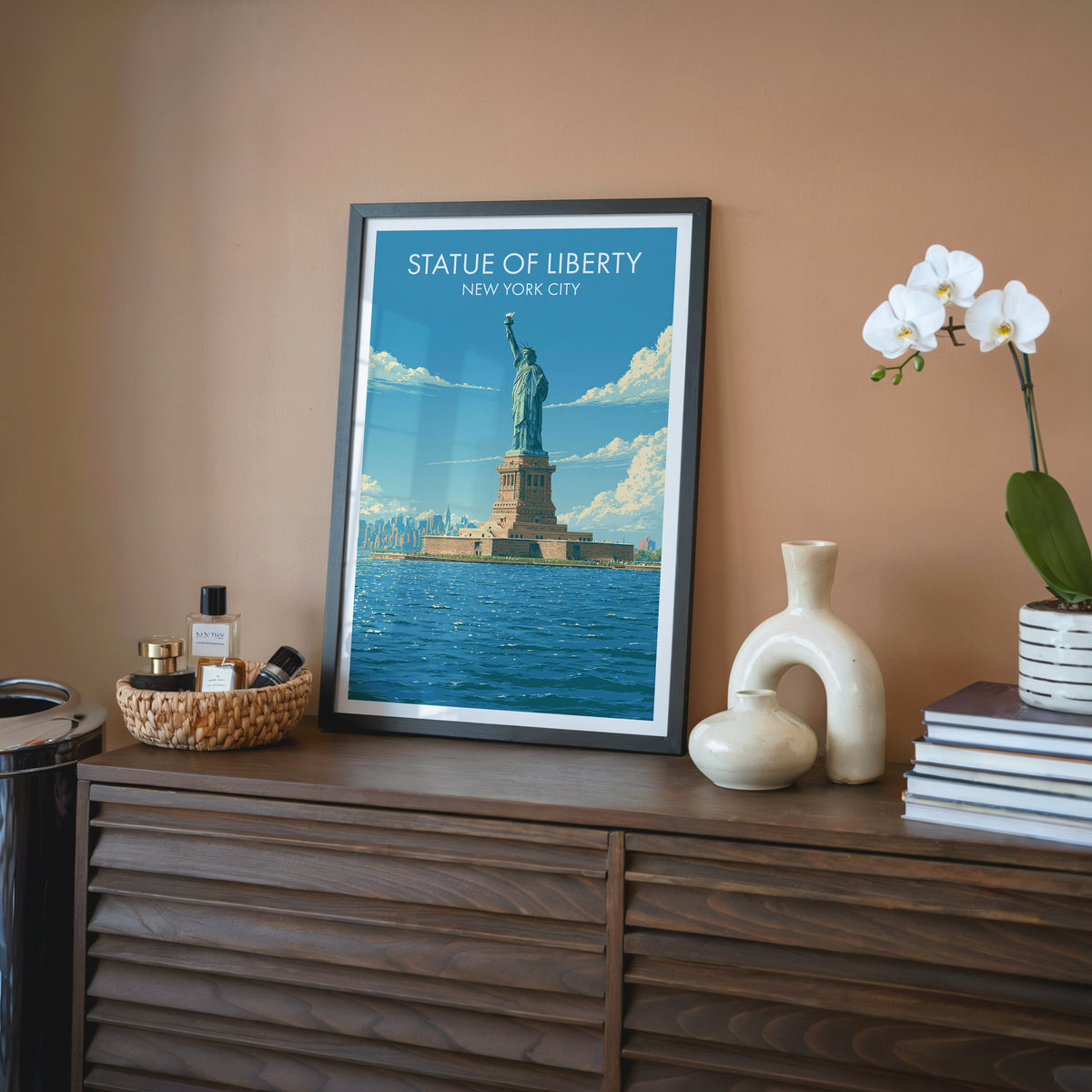 Liberty Island wall art in a black frame on a walnut sideboard against terracotta, with a cream ceramic vase.