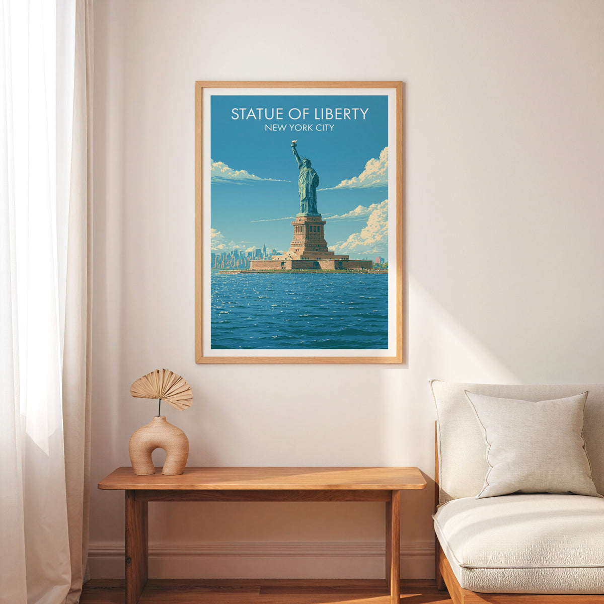 Statue of Liberty poster in an oak frame above a slim wood bench, cream armchair and a palm-leaf fan.