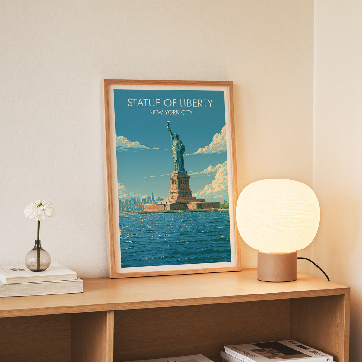 Slim oak-framed Statue of Liberty print on an oak console beside a round lamp and daisies in a glass jar.