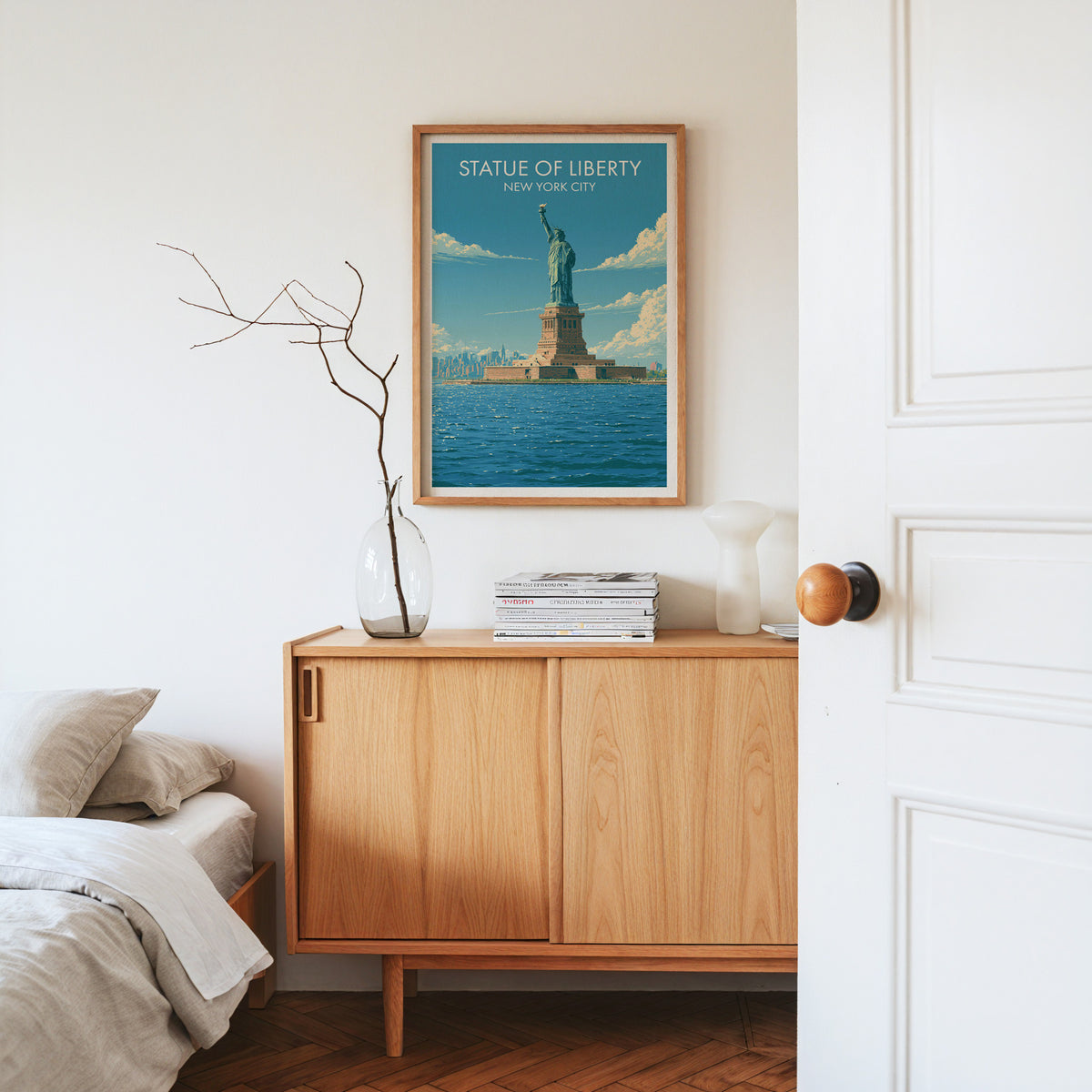 Statue of Liberty print in an oak frame on a pale oak sideboard with dried branches and a white vase.