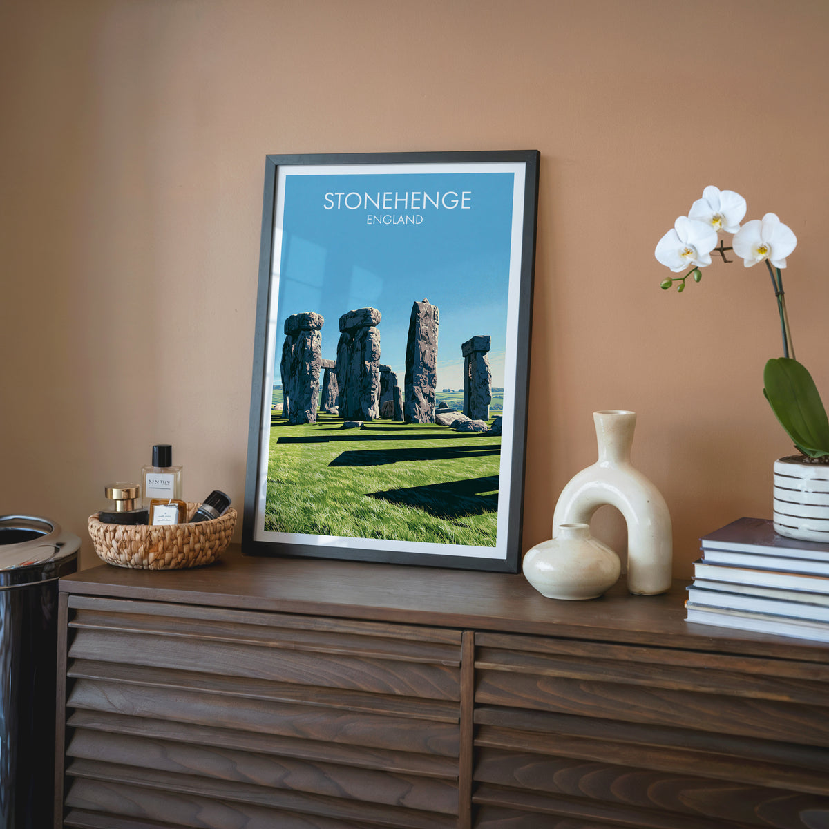 England landscape wall art, black frame on a walnut sideboard against a terracotta wall with an orchid