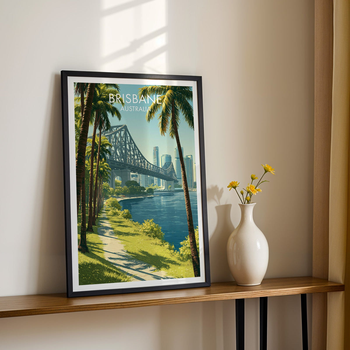 Story Bridge river print in a black frame on a wood shelf with yellow daisies against a sunlit cream wall