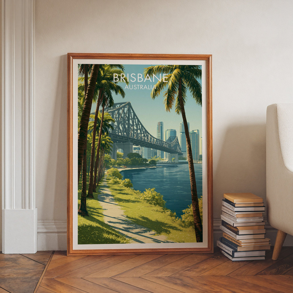 Story Bridge travel print in a walnut frame on herringbone floor beside stacked books and a pale armchair