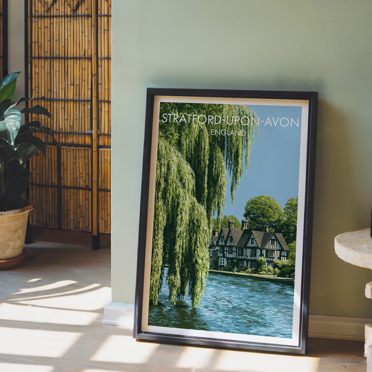 Avon riverside poster, dark frame leaning on a sage-green wall beside a bamboo screen and a peace lily