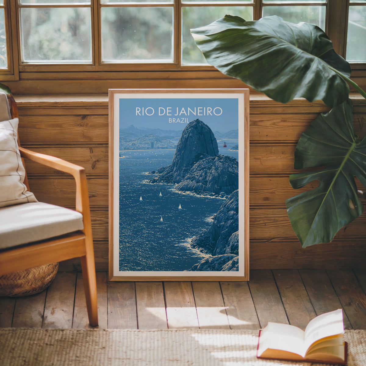 Granite peak travel print in an oak frame against a pine cabin wall with a wood chair, monstera leaf and open book