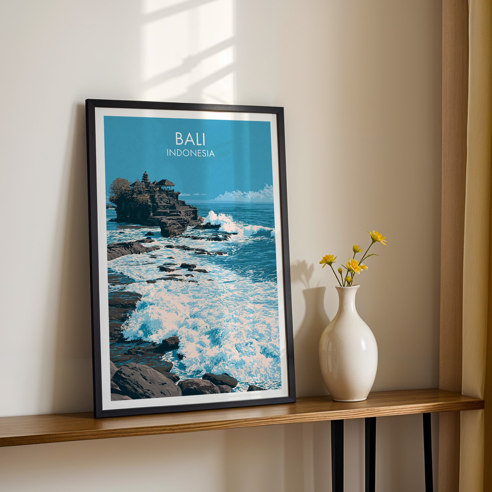 Black framed Tanah Lot Bali Indonesia print on a narrow hallway console in sunlight, styled with yellow flowers