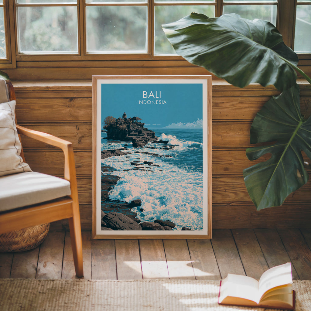 Framed Tanah Lot Bali Indonesia poster leaning against a timber cabin wall with monstera leaves and an open book